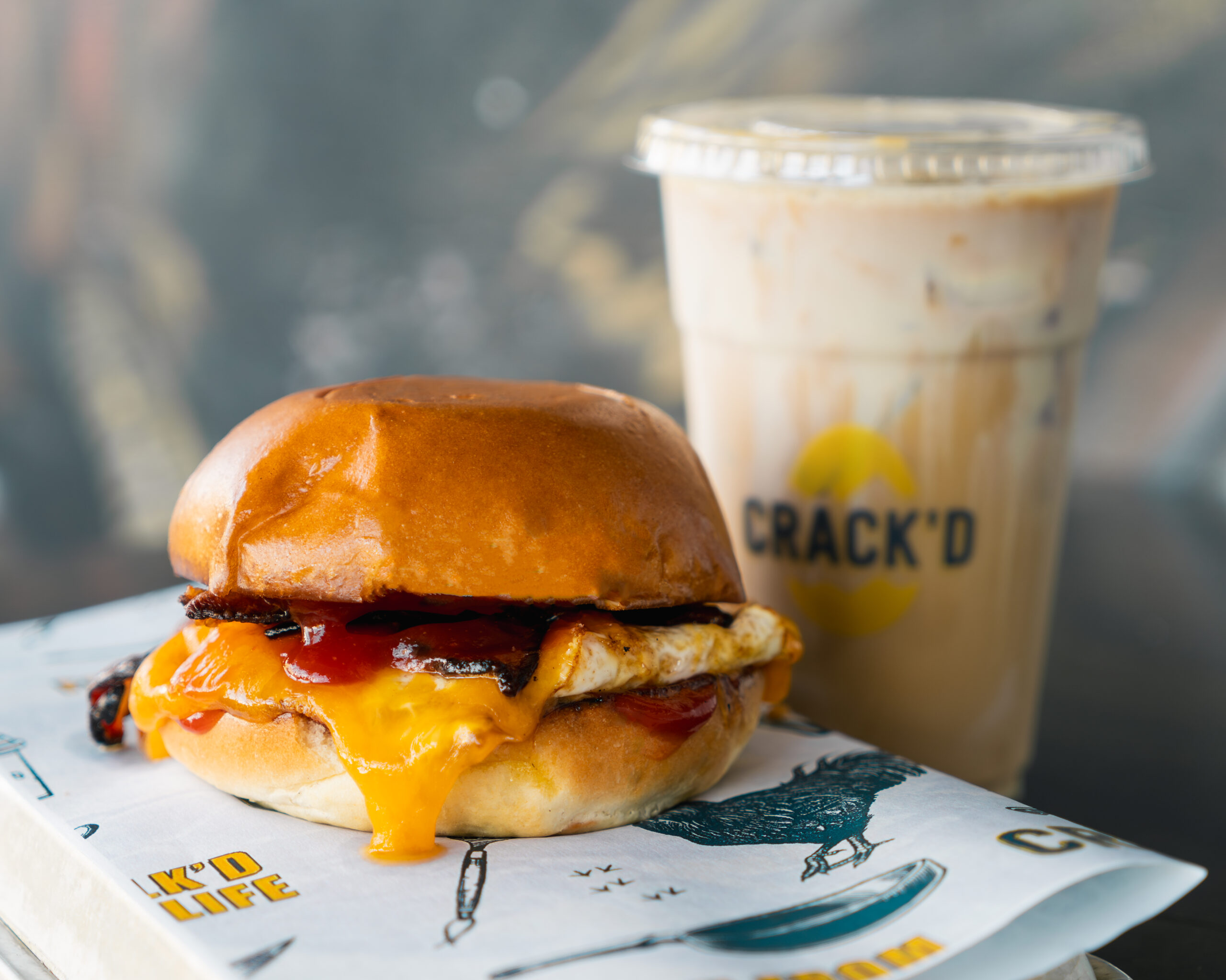 Breakfast sandwich with egg, cheddar cheese, and sauce, paired with a drink from CRACK’D.