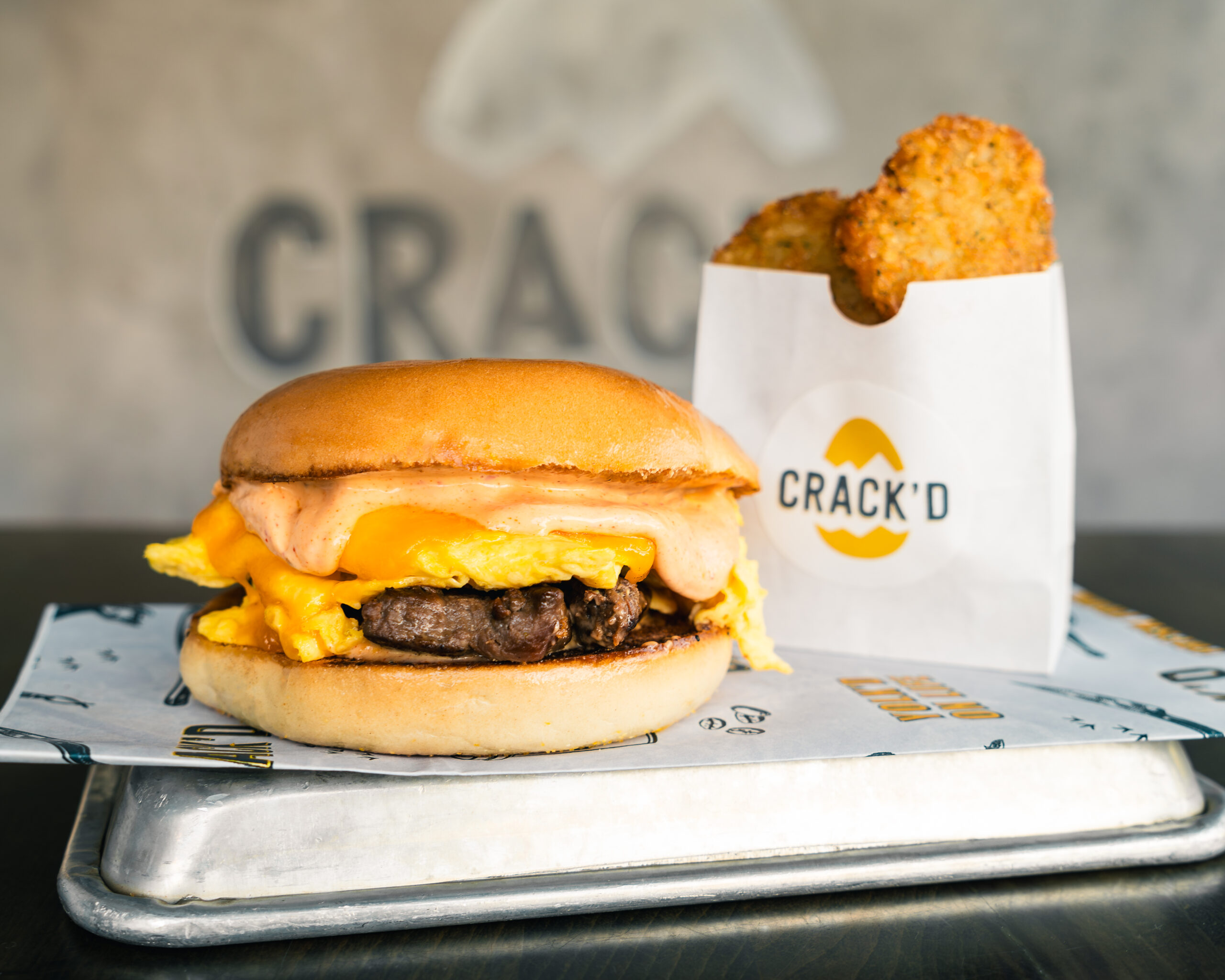 Burger with meat, caramelized onions, and egg, served on a tray in a casual setting.