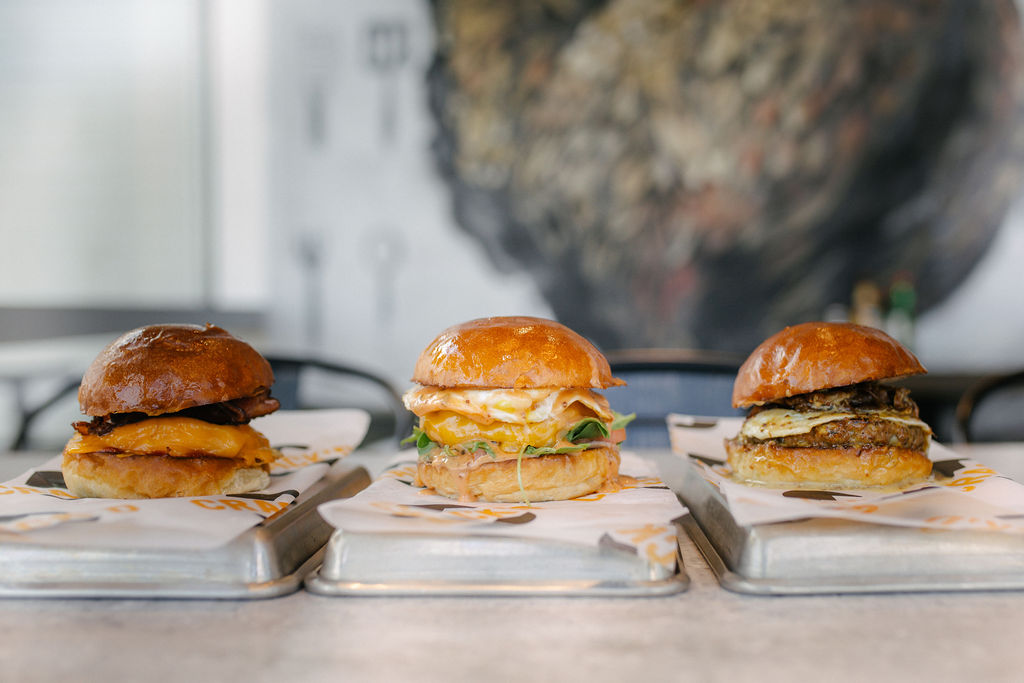 Three burgers on metal trays in a modern setting.
