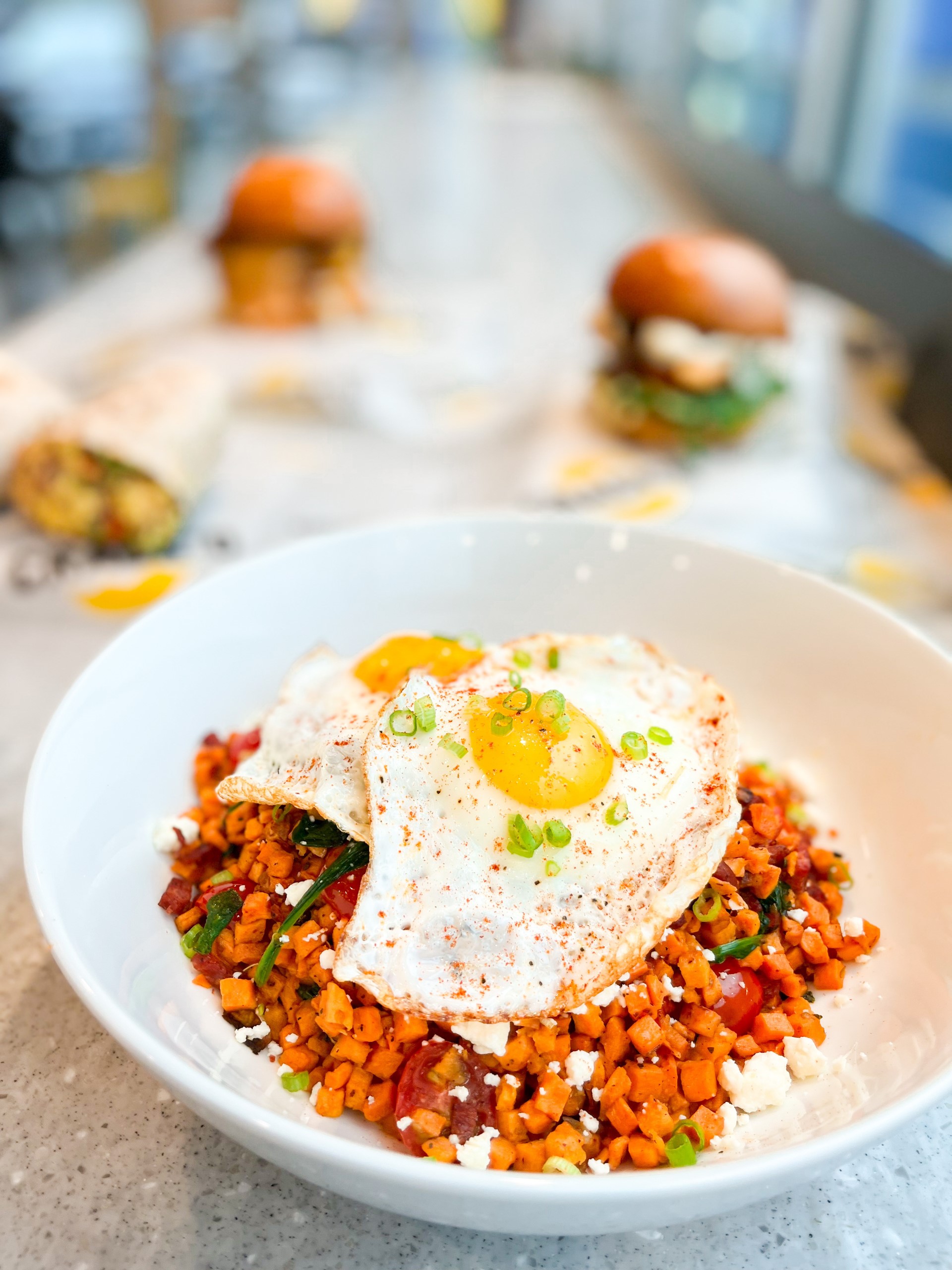 Bowl with two fried eggs, presented on a table with burgers in the background.